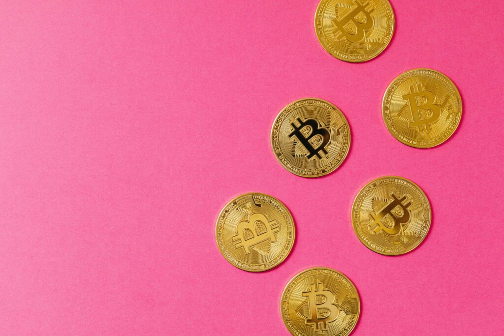 Gold Bitcoin coins on a vibrant pink surface, representing cryptocurrency and blockchain investment.